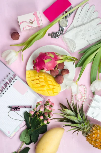 Women\'s accessories in white and pink colors whith tropical fruits. Mango, pineapple, pitahaya, lychee, flowers, notebook with pen, cosmetics and gift boxes. Beauty women flat lay. Top view.