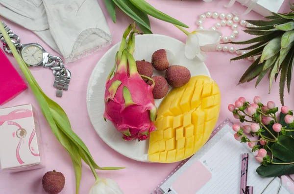 Women's accessories in white and pink colors whith tropical fruits. Mango, pineapple, pitahaya, lychee, flowers, notebook with pen, cosmetics and gift boxes. Beauty women flat lay. Top view.