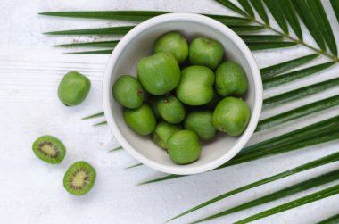 Beyaz tabakta mini kivi. Beyaz arka planda küçük egzotik meyveler.