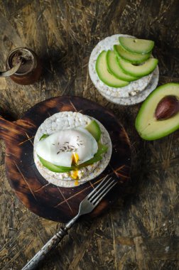 Krem peynir, avokado ve siyah arka plan üzerinde haşlanmış yumurta ile Pirinç kek. Sandviçli sağlıklı kahvaltı.