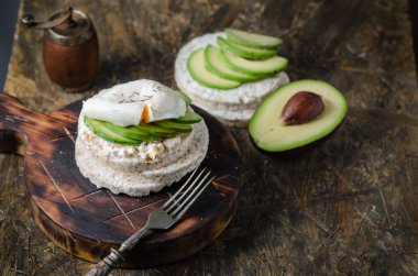 Krem peynir, avokado ve siyah arka plan üzerinde haşlanmış yumurta ile Pirinç kek. Sandviçli sağlıklı kahvaltı.