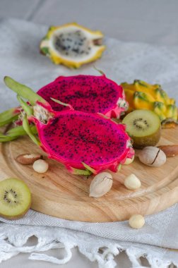 Çeşitli ejderha meyve - sarı ve kırmızı pitahaya, sarı kivi ve fındık ahşap bir tepsi üzerinde