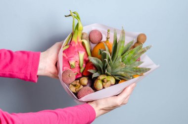 Yenilebilir aranjmanlar, yenilebilir egzotik meyve buketi. Ananas, granadilla, litchi, çilek, pide, mangosten pembe elbiseli bir kadının elinde.
