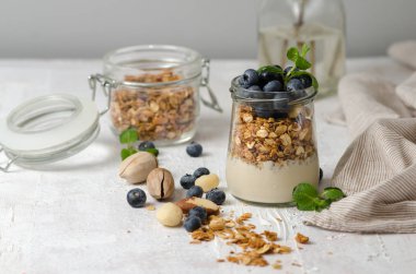 Sağlıklı kahvaltı - taze yaban mersini, yoğurt, fındık ve nane ile granola cam kavanoz. Açık arka planda Granola, metin için alan.