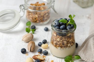 Sağlıklı kahvaltı - taze yaban mersini, yoğurt, fındık ve nane ile granola cam kavanoz. Açık arka planda Granola, metin için alan.
