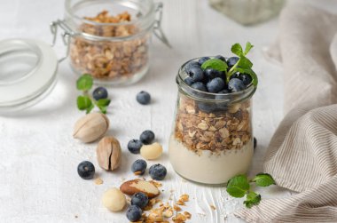 Sağlıklı kahvaltı - taze yaban mersini, yoğurt, fındık ve nane ile granola cam kavanoz. Açık arka planda Granola, metin için alan.