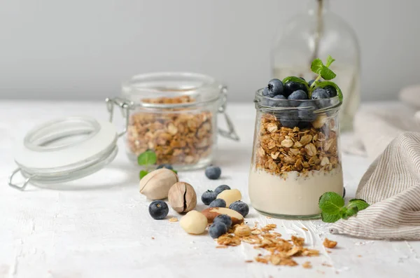 Hälsosam frukost-glas burkar granola med färska blåbär, yoghurt, nötter och mynta. Granola på en ljus bakgrund, utrymme för text. — Stockfoto