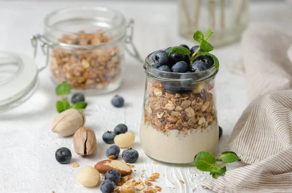 Hälsosam frukost-glas burkar granola med färska blåbär, yoghurt, nötter och mynta. Granola på en ljus bakgrund, utrymme för text. — Stockfoto