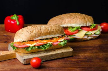 Siyah arka plan üzerinde ahşap bir tahta üzerinde jambon, salam, peynir, havuç, domates, kırmızı peper ve salata ile iki lezzetli sandviç. Metin için alan