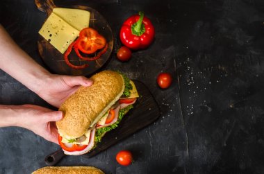 Taze sebze dolu ahşap bir masada jambon, peynir, kırmızı biber, mantar ve salata ile lezzetli sandviçler. Elinde sandviç