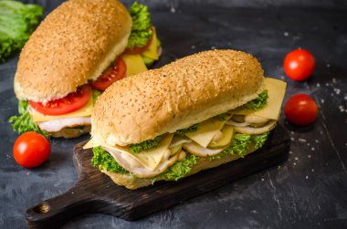 Siyah arka plan üzerinde ahşap bir tahta üzerinde jambon, peynir, domates, tuzlu salatalık ve salata ile iki lezzetli sandviç.