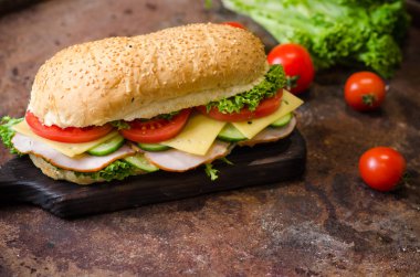 Eski arka planda ahşap bir tahta üzerinde jambon, peynir, domates ve salata ile lezzetli sandviçler