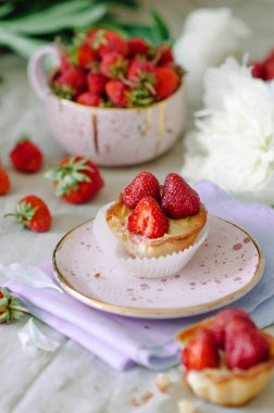 Çilek ve muhallebi ile Tartlet. Masada çiçekler ve çilekler, pembe seramik tabaklar.