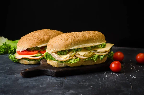 两个美味的三明治，火腿，奶酪，西红柿，咸黄瓜和沙拉在一块黑板上，在黑色背景。文本空间 — 图库照片