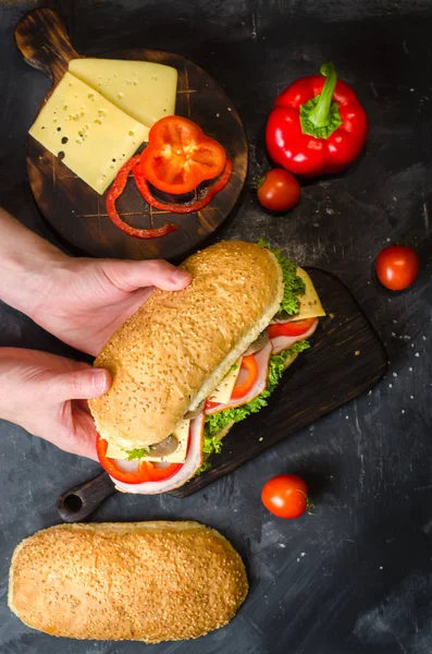 Pyszne kanapki z szynką, serem, czerwonym pieprzem, grzybami i sałatką na drewnianym stole pełnym świeżych warzyw. Kanapka w ręku — Zdjęcie stockowe