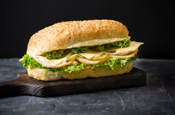 Siyah arka plan üzerinde ahşap bir tahta üzerinde jambon, peynir, tuzlu salatalık ve salata ile lezzetli sandviçler.