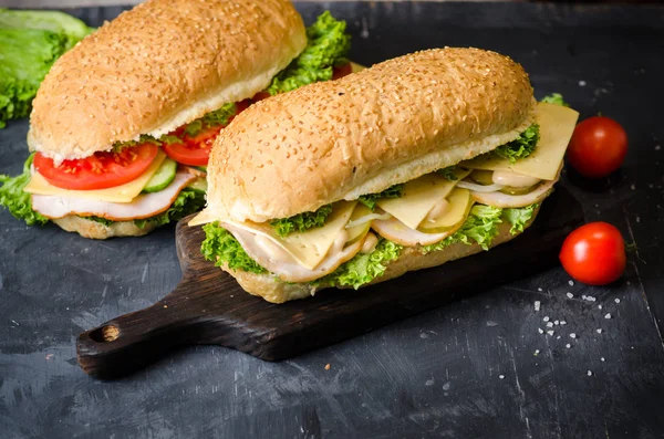 两个美味的三明治，火腿，奶酪，西红柿，咸黄瓜和沙拉在黑板上的黑色背景. — 图库照片