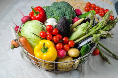 Masanın üstündeki metal sepette taze sebzeler. Kiraz domates, kuşkonmaz, brokoli, patates, biber, turp, patlıcan, kabak, havuç ve soğan.