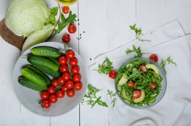 Salatalık, kiraz domates, arugula, avokado, beyaz arka plan üzerinde bebek mısır ile taze salata. Odun üstünde sebzeler. Bio Sağlıklı gıda, otlar ve baharatlar. Ahşap üzerinde organik sebzeler.