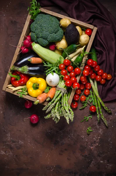 Box with farm vegetables on a dark background. Place for text. Cherry tomatoes, asparagus, broccoli, peppers, eggplants, zucchini, carrots and onions. — Stock Photo, Image