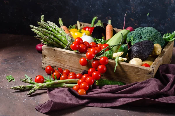Caja con verduras de granja sobre un fondo oscuro. Lugar para el texto. Tomates cherry, espárragos, brócoli, pimientos, berenjenas, calabacines, zanahorias y cebollas . —  Fotos de Stock