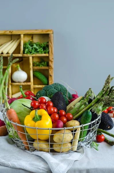 Legume proaspete într-un coș de metal pe masă. Roșii cireșe, sparanghel, broccoli, cartofi, ardei, ridiche, vinete, dovlecei, morcovi și ceapă . — Fotografie, imagine de stoc