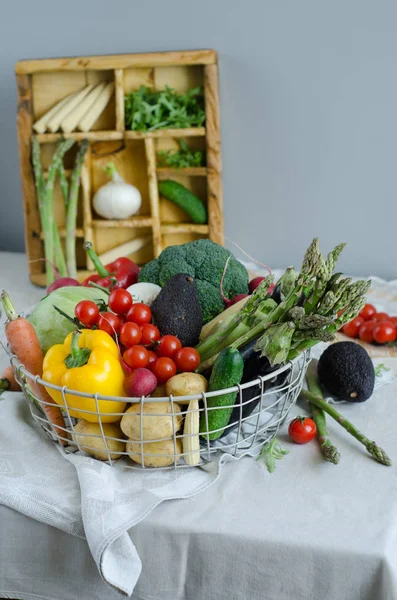 Φρέσκα λαχανικά σε ένα μεταλλικό καλάθι στο τραπέζι. Ντοματίνια, σπαράγγια, μπρόκολο, πατάτα, πιπεριές, ραπανάκια, μελιτζάνες, κολοκυθάκια, καρότα και κρεμμύδια. — Φωτογραφία Αρχείου