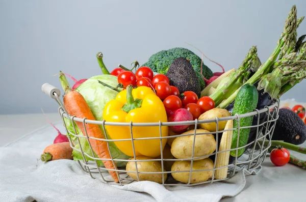 Fresh vegetables in a metal basket on the table. Cherry tomatoes, asparagus, broccoli, potato, peppers, radish, eggplants, zucchini, carrots and onions. — Stock Photo, Image