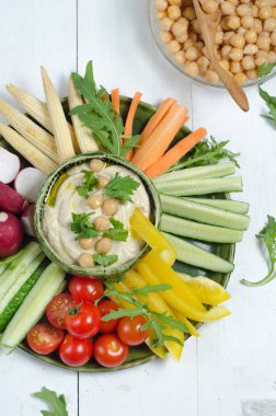 Çeşitli aperatifler ile humus tabağı. Kasede humus, sebze çubukları, nohut, zeytinyağı. Sebzeler, humus sosu, kopya alanı. Üst te. Beyaz ahşap arka plan