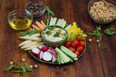 Çeşitli aperatifler ile humus tabağı. Kasede humus, sebze çubukları, nohut, zeytinyağı. Sebzeler, humus sosu, kopya alanı. Koyu ahşap arka plan