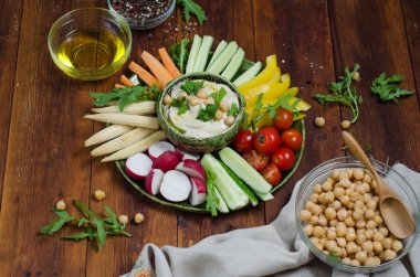 Çeşitli aperatifler ile humus tabağı. Kasede humus, sebze çubukları, nohut, zeytinyağı. Sebzeler, humus sosu, kopya alanı. Koyu ahşap arka plan