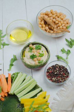 Çeşitli aperatifler ile humus tabağı. Kasede humus, sebze çubukları, nohut, zeytinyağı. Sebzeler, humus sosu, kopya alanı. Beyaz ahşap arka plan