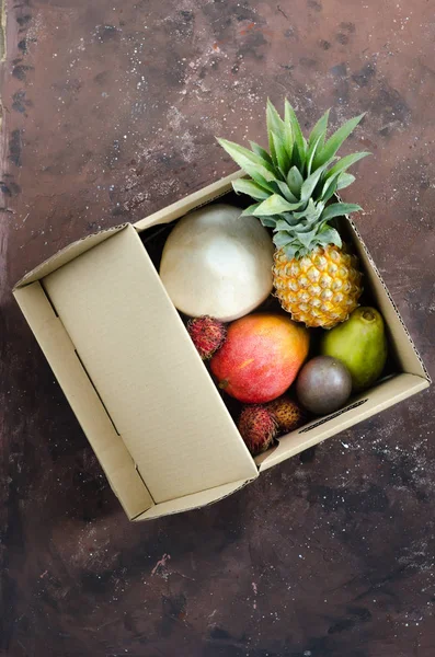 Tropical fruit delivery in a cardboard box. Fruits on a dark background. Top view