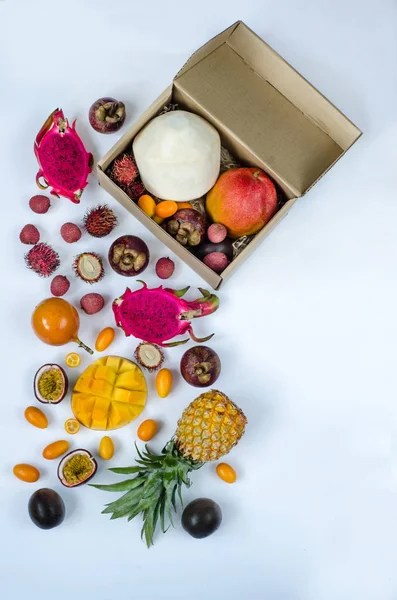 Healthy eating, varieity of exotic fruits on a white background, vertical top view. Tropical fruits whole and sliced. Fruit delivery in a cardboard box