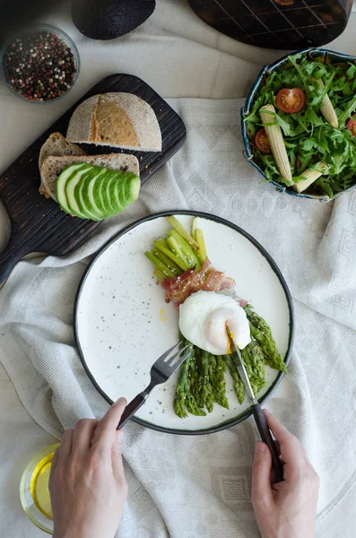 Colazione sana - asparagi verdi avvolti con pancetta, uova in camicia benedetto, insalata e pane tostato con avocado. Colazione su un tavolo leggero con tovaglia . — Foto Stock