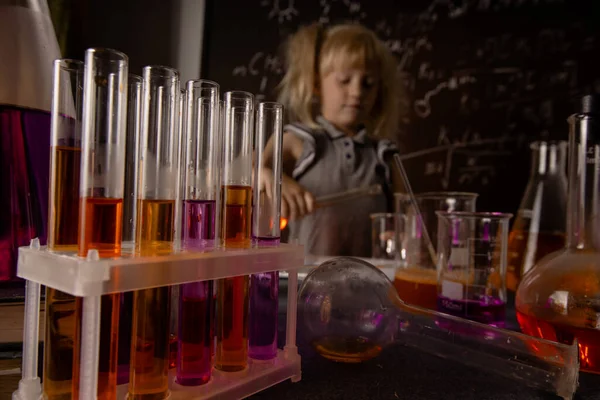 Curious little girl with test tubes and colorful substances makes tests at school laboratory. Small kid learning chemistry. Selective focus. Biology education concept.
