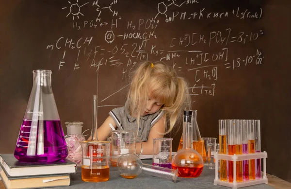 Curious little girl with test tubes and colorful substances makes tests at school laboratory. Small kid learning chemistry and conducts science experiment on biology lesson. Biology education concept.