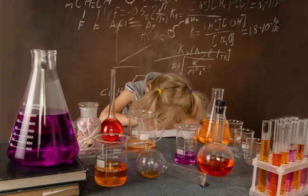 Curious little girl with test tubes and colorful substances is tired to conduct science experiment on biology lesson.. Small kid sleeping on biology lesson. Science and education concept.