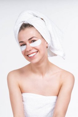 white girl sticks patch for eyes. Nude in a towel on the chest and head. Without make-up, natural. on an empty background. Portrait. Pretty smile. White teeth