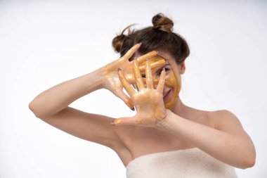 young girl in a cosmetic mask for the face of gold color posing. Shows a different mood. Cheerful, sad, mysterious. Portrait on a blank white background. hands in the frame.