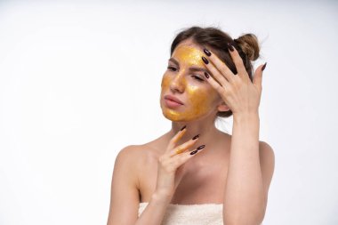 Avrupalı kız 25 yaşında altın renkli bir yüz maskesi koyar. Nemlendirici yüz maskesi. İyi bir ruh halinde. Yüz cilt bakımı.