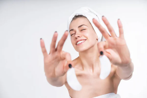 Young naked girl in a towel shows patches for the eyes. Laughs happily. Happy Portrait on a blank background. Facial treatment. Skin care. — Stock Photo, Image