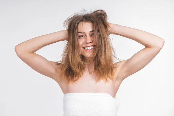 young nude girl in a towel with disheveled hair looks into the camera. Shows armpits. Shaved armpits. Beautiful smile, white teeth. Cheerful, mischievous. On an empty background.