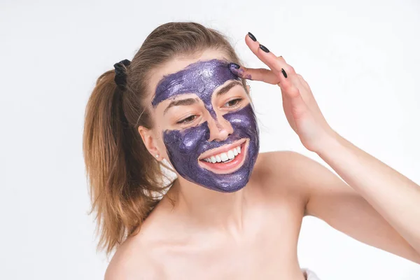 Potret gadis cantik dengan jari-jarinya menempatkan di wajahnya topeng kosmetik ungu. Eropa, 22 tahun, putih, latar belakang kosong — Stok Foto