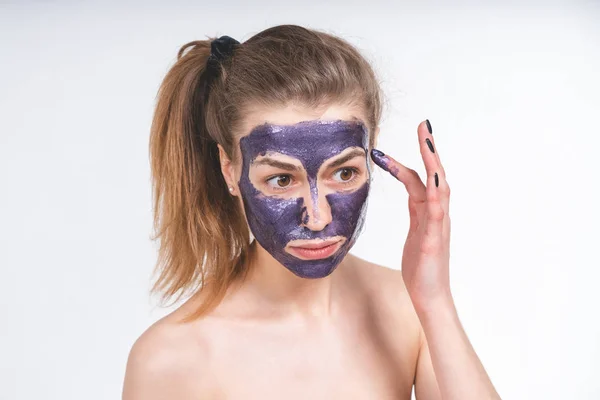 Potret gadis cantik dengan jari-jarinya menempatkan di wajahnya topeng kosmetik ungu. Eropa, 22 tahun, putih, latar belakang kosong — Stok Foto
