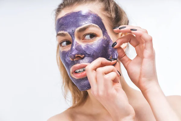 Gadis muda dengan wajah cantik menghilangkan topeng kosmetik ungu. Close-up. Makro . — Stok Foto