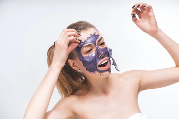 Giovane bella ragazza rimuove una maschera cosmetica viola, patch. Si separa parzialmente. Primo piano. Macro. Ritratto emotivo. Cura del viso, procedure . — Foto Stock