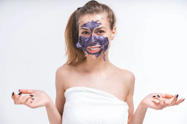 Una bella ragazza bianca nuda, di 22 anni, avvolta in un asciugamano, toglie una maschera cosmetica viola dal suo viso. E 'lacerato. Il piano medio. Ritratto emotivo . — Foto Stock