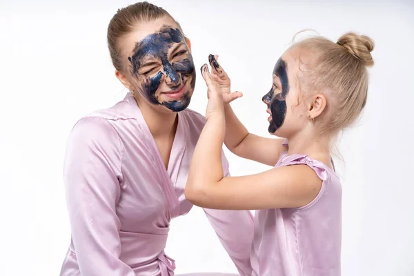Petite fille fait de sa mère un masque cosmétique sur son visage. La fille se soucie, aide maman. Petite fille et jeune mère . — Photo
