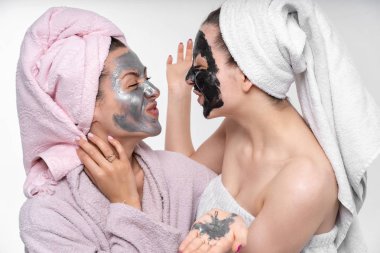 Kız kız kardeşine kozmetik bir maske takıyor. Onlar eğlenmek ve sürecinde şımartın. Boş arka plan, harika bir ruh hali. Yüz cilt bakımı. Kız kardeş.